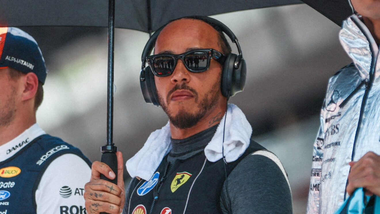 Lewis Hamilton holding an umbrella as he stands on the grid wearing earphones