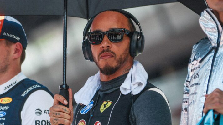 Lewis Hamilton holding an umbrella as he stands on the grid wearing earphones
