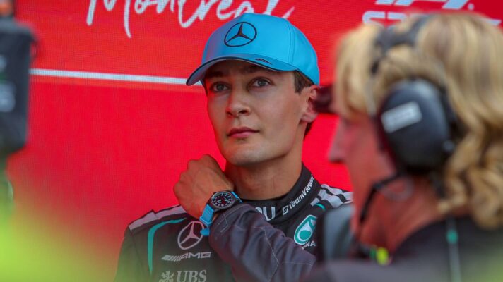 George Russell adjusts his collar against a red background in parc ferme