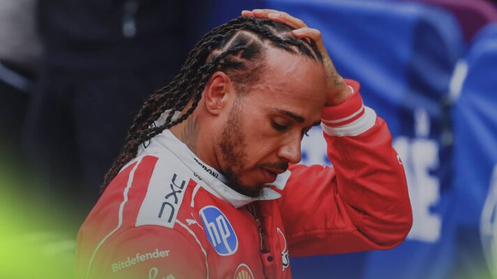 A tired Lewis Hamilton holds his hand on his head in parc ferme as he looks downwards