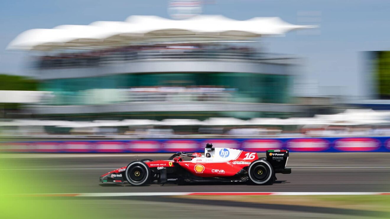 An action shot of Charles Leclerc's Ferrari on track at Brooklands at Silverstone with the BRDC building in the background