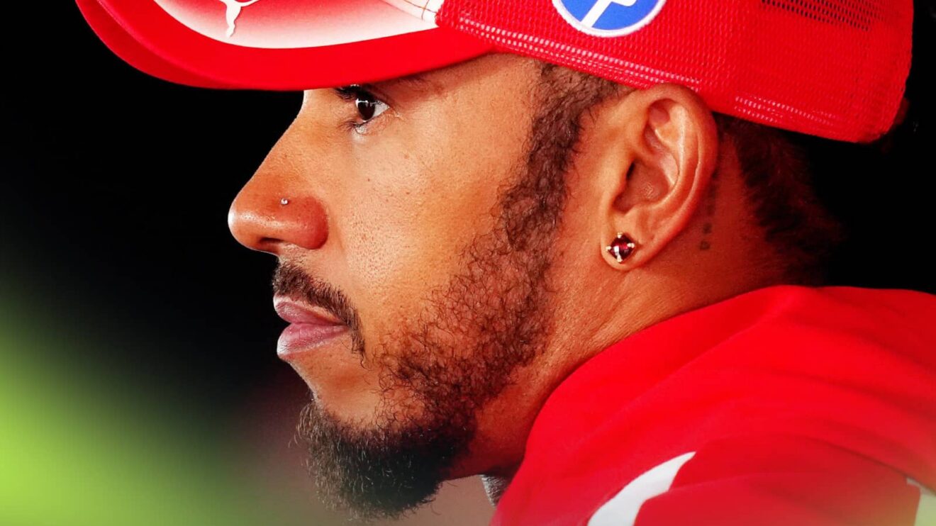 A side-profile shot of Lewis Hamilton wearing a red Ferrari cap and hoodie against a black background
