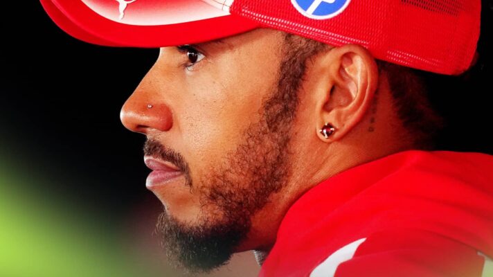 A side-profile shot of Lewis Hamilton wearing a red Ferrari cap and hoodie against a black background