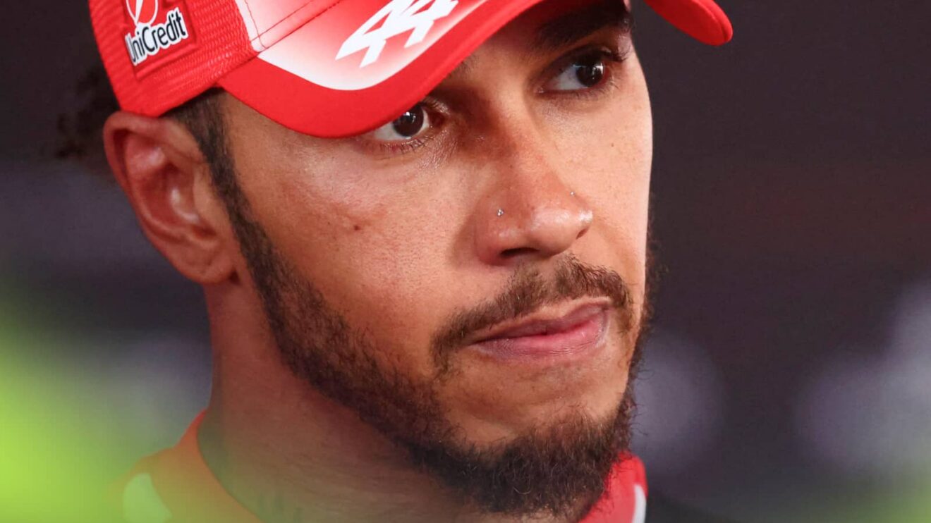 A close-up shot of Lewis Hamilton facing the media while wearing a red Ferrari cap