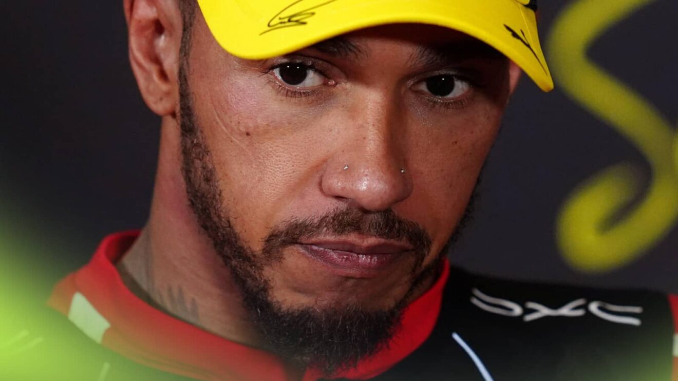 A close-up shot of Lewis Hamilton looking on in a press conference while wearing a yellow cap