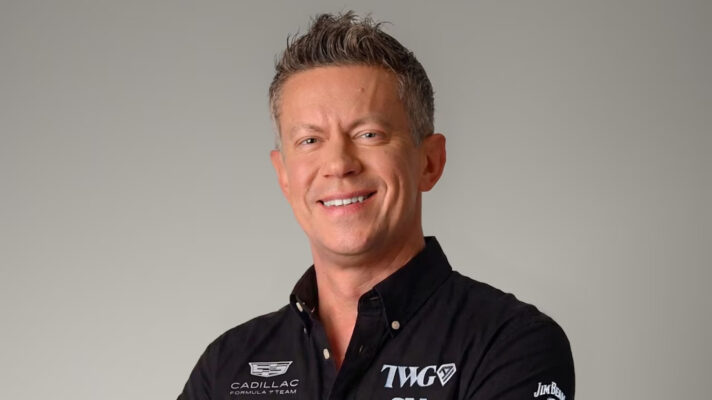 Marcin Budkowski smiles while wearing a black Cadillac team shirt against a grey background