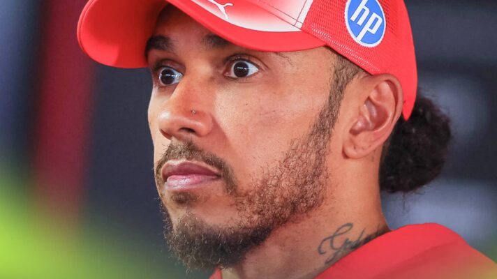 Lewis Hamilton stands with his eyes wide as he faces questions from the media
