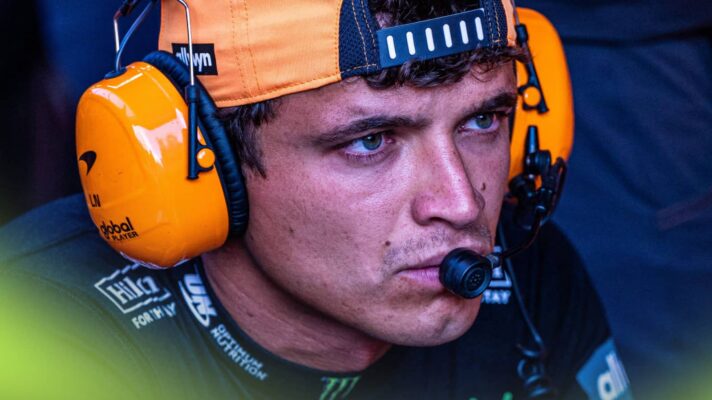 Lando Norris looks intense while wearing a set of headphones in the McLaren garage