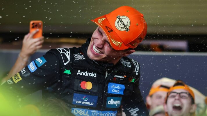 Lando Norris smiles with champagne droplets in the air as he celebrates in the pit lane