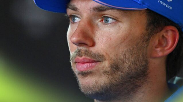 Pierre Gasly wearing a blue Alpine cap against a dark background