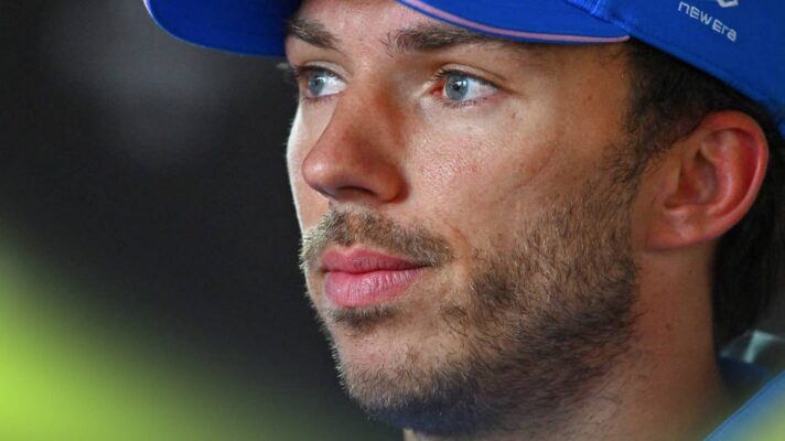 Pierre Gasly wearing a blue Alpine cap against a dark background