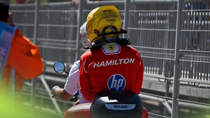 A rear-facing shot of Lewis Hamilton wearing his red Ferrari race suit and yellow helmet on the back of a motorbike in Madrid