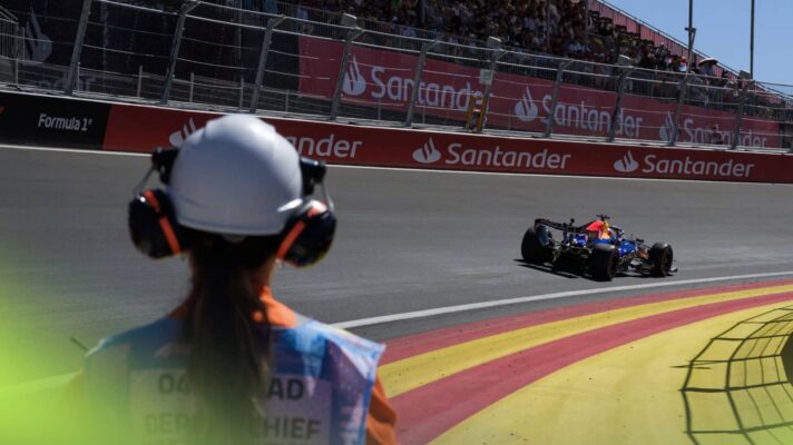 A rear-facing view of a long-haired marshal watching on as Max Verstappen's Red Bull negotiates the banked La Monumental corner in Madrid