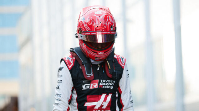 Esteban Ocon walking through the paddock with his head down and his helmet on