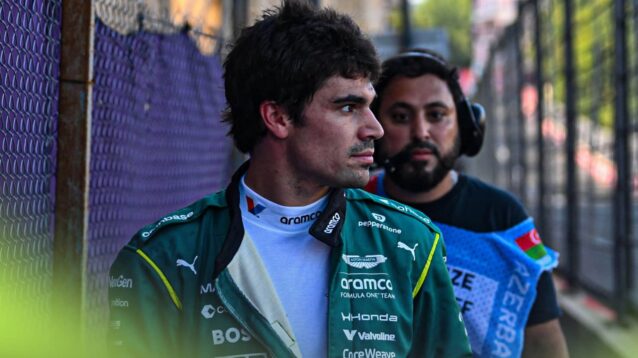 Lance Stroll looks out on to the track from behind a safety fence in Baku with a marshal behind him