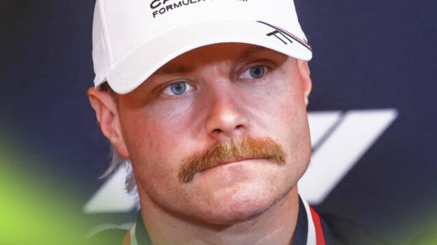 A close-up shot of Valtteri Bottas wearing a black Cadillac jacket and white cap in a press conference
