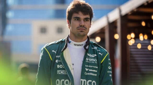 Lance Stroll walks through the F1 paddock with his Aston Martin overalls unzipped.