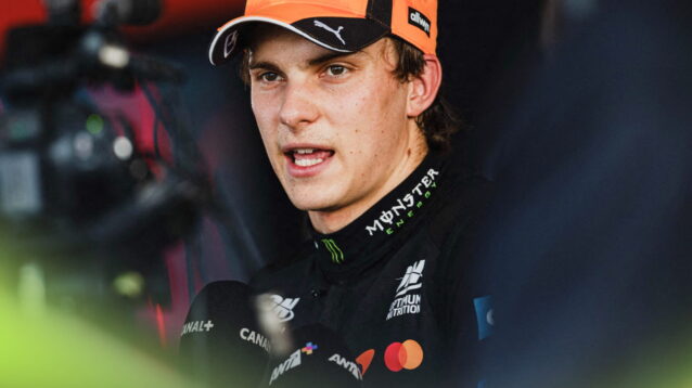 Oscar Piastri speaks to the media while wearing an orange McLaren cap and black fireproof underwear