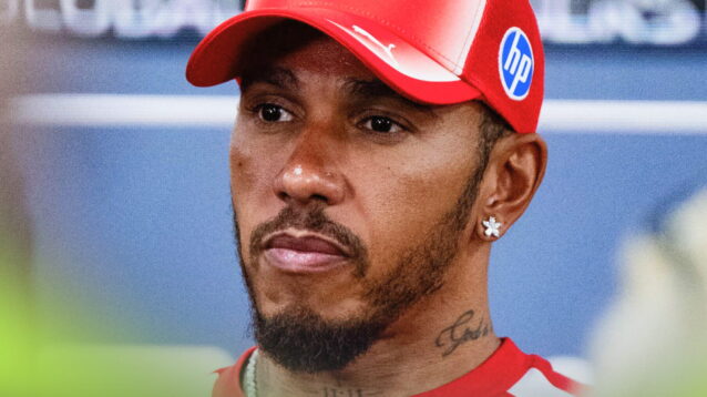 Lewis Hamilton looks on while facing the media while wearing a red Ferrari cap and t-shirt