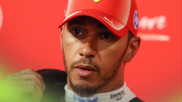 Lewis Hamilton wearing a red cap with a towel over his shoulder and bright-red Ferrari branding in the background