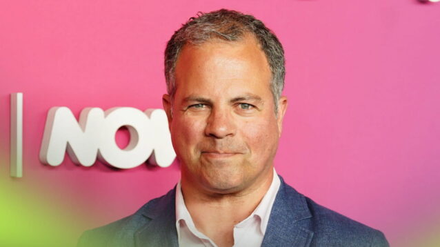 Ted Kravitz directly eyes the camera while wearing a suit against a bright-pink background